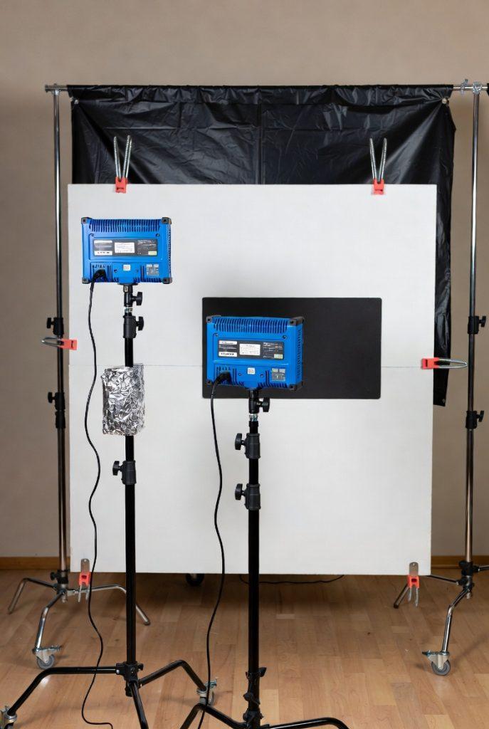 Visual guide to building a functional low-budget lighting kit: two adjustable bi-color LED panels (~$150 total) on light stands for key/fill, white foam core boards (~$20) as bounce and diffusion surfaces, black cinefoil (~$15) and fabric for negative fill and flags, spring clamps (~$10), and parchment paper or fabric diffusion (~$15), arranged to create three-point lighting with natural bounce options—no gels required thanks to bi-color temperature control—perfect for beginners learning motivated, controlled lighting.