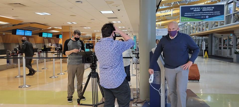 Low-budget short film - Film crew at work in an airport terminal departure area, featuring actors, director, and assistant director coordinating a scene.