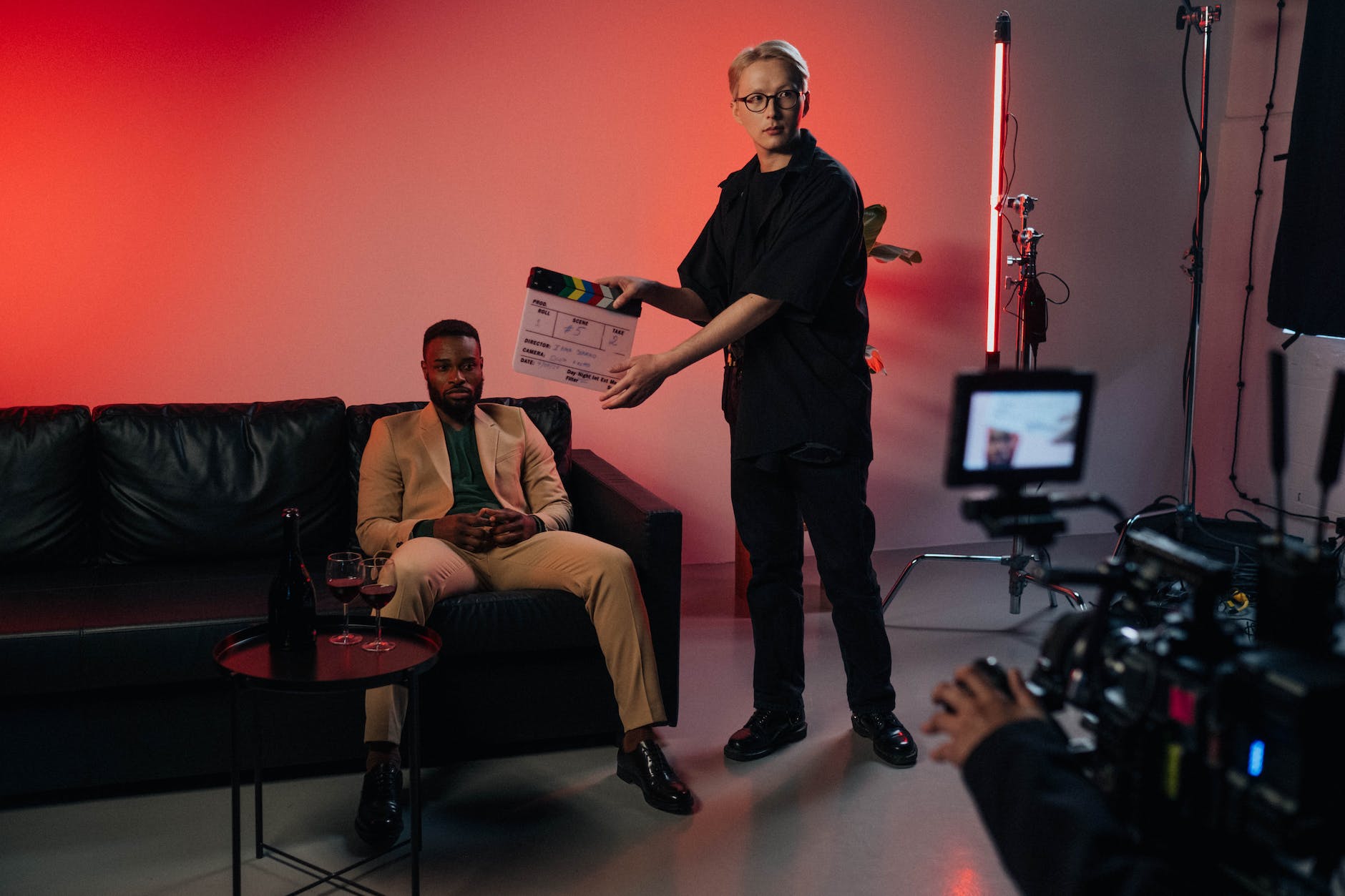 a man in black t shirt holding holding a clapperboard near a man sitting on black sofa