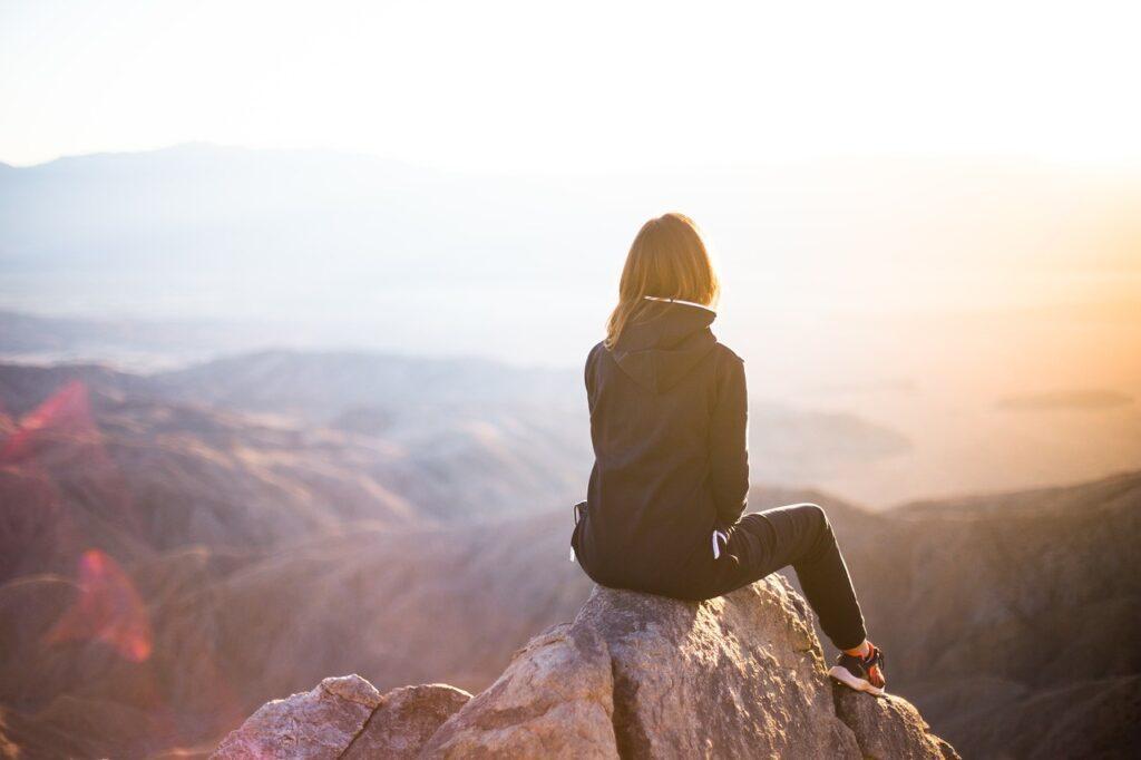 solo travel vlogging woman sitting on mountain overlooking valley