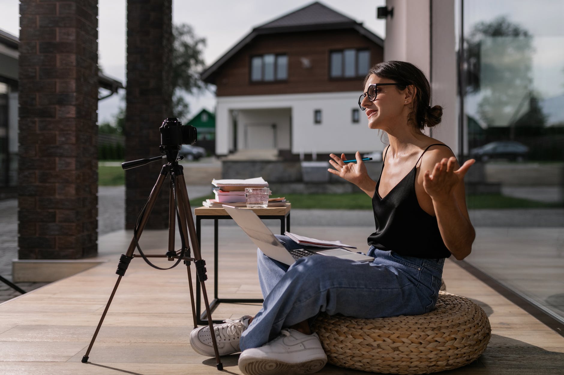 Filmmaker vlogging Beginner Vloggers woman in black tank top and blue denim jeans sitting on brown wicker ottoman