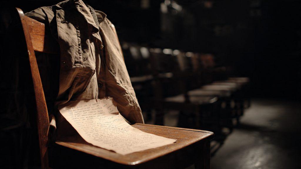 A single, stark spotlight on a simple wooden chair in an empty, dark theater. Hanging on the back of the chair is not a costume, but a well-worn, everyday jacket. Resting on the seat is a script with handwritten notes in the margins. The atmosphere is anticipation and quiet power. Moody, high contrast, evocative.