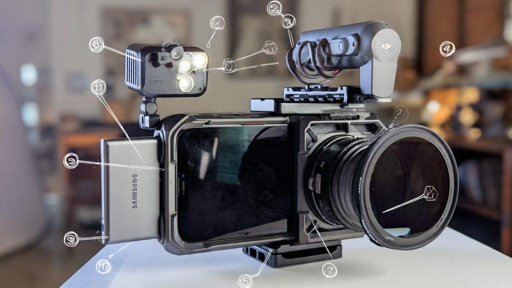 *Technical illustration-style photograph. A smartphone mounted in the Moment SuperCage. The Samsung T9 SSD attached via MagSafe plate to the back. PolarPro VND filter threaded onto the lens. A DJI Mic 2 transmitter clipped to the top NATO rail. The SmallRig RM120 positioned off to the side, bouncing off a white foam core board. Annotated with numbered callouts. No stylized lighting—flat, documentary, functional.*