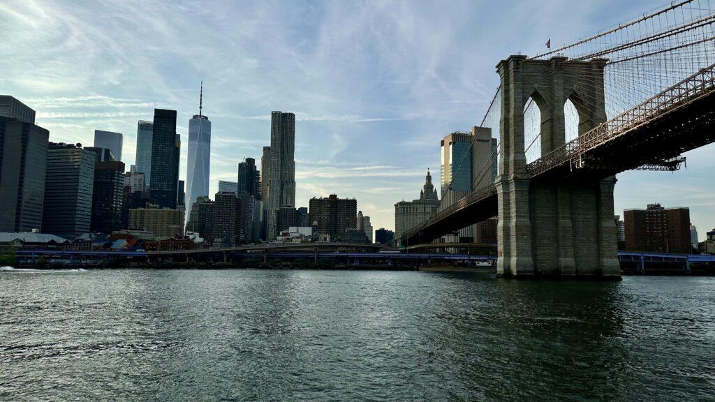 A breathtaking view of the Brooklyn Bridge from a NYC ferry, with the iconic One World Trade Center soaring majestically in the background.