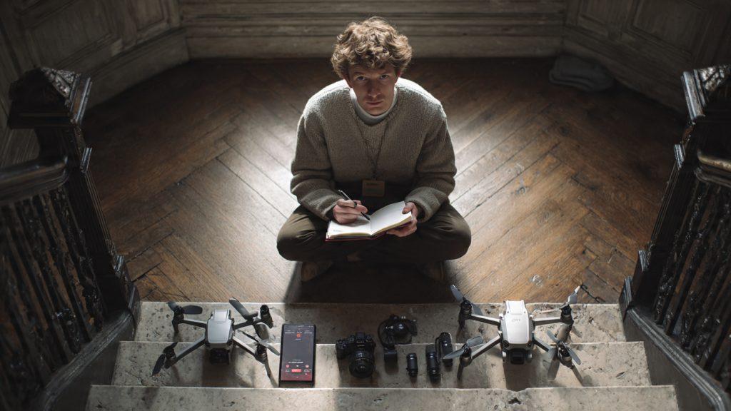 Filmmaker sitting on a location staircase with a notebook, four DJI products laid out in front: OM 6, Mini 4 Pro, Mic 2, Pocket 3, pen in hand mid-decision, thoughtful expression, natural window light, photorealistic