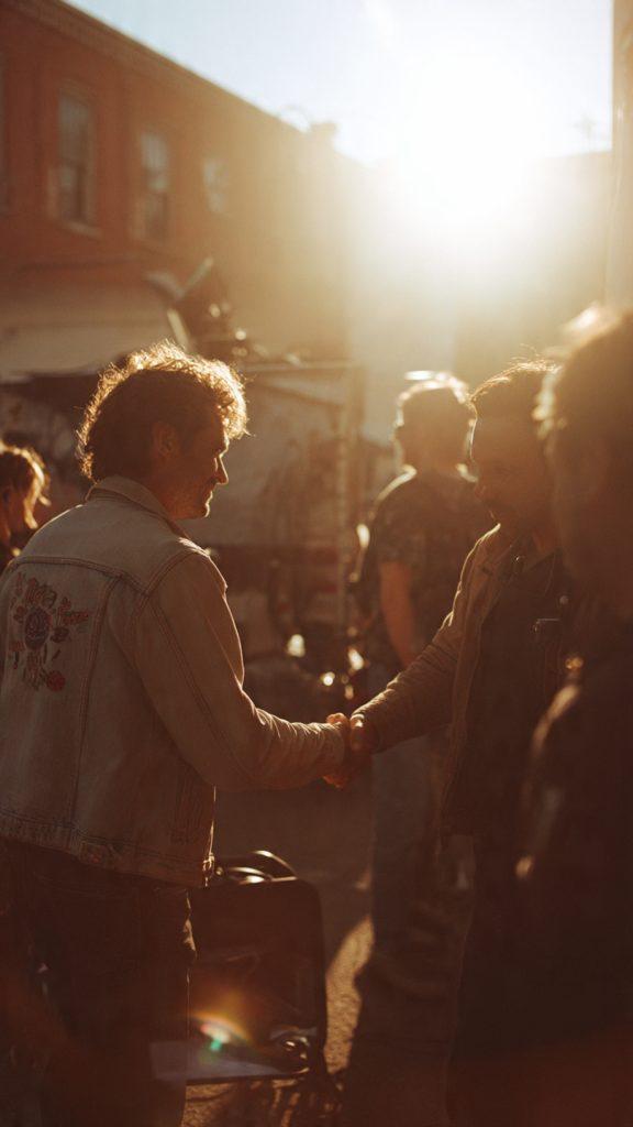 life lessons Quiet moment on a film set during wrap—DP and director shaking hands, crew packing equipment in soft golden hour light, genuine human connection, candid documentary photography