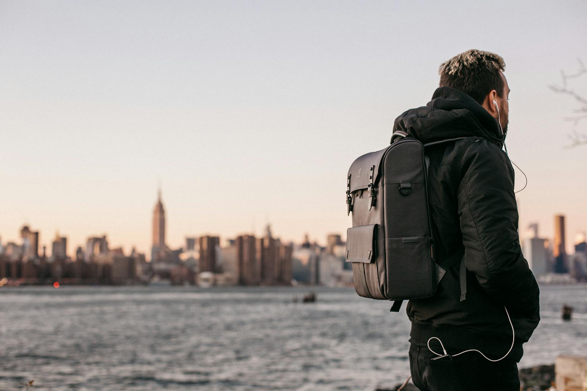 backpack filmmaking man wearing black bubble jacket and black leather backpack near bay