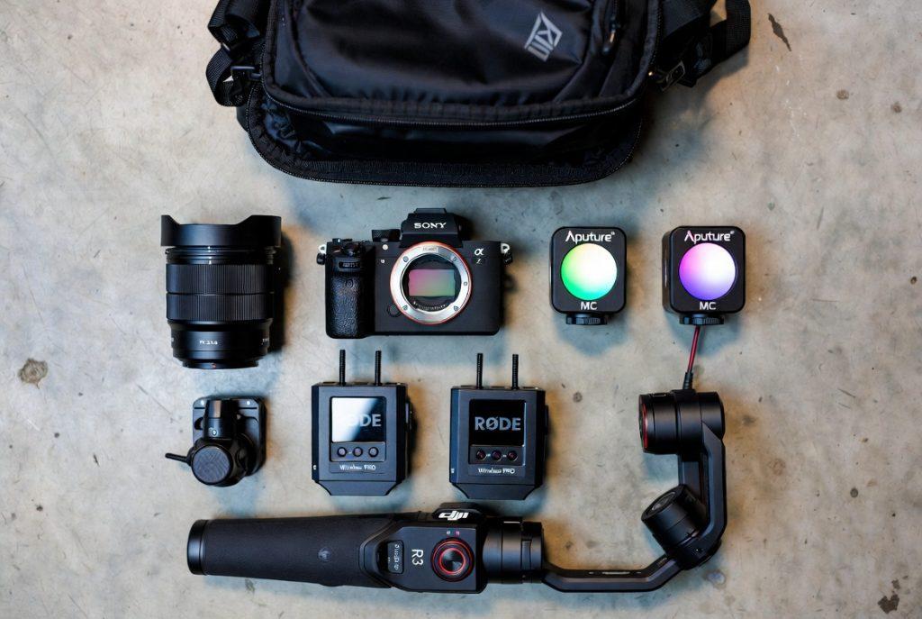 "Guerrilla filmmaking kit laid out on location" — Overhead flat-lay of the complete Sony A7S III setup: camera body, 35mm lens, Aputure MC lights, Rode Wireless PRO transmitters, DJI RS 3 Mini gimbal, all fitting inside Peak Design Everyday Backpack. Shot on industrial concrete floor.
